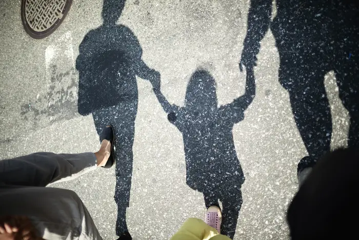 The shadow of a child holding hands with two adults.